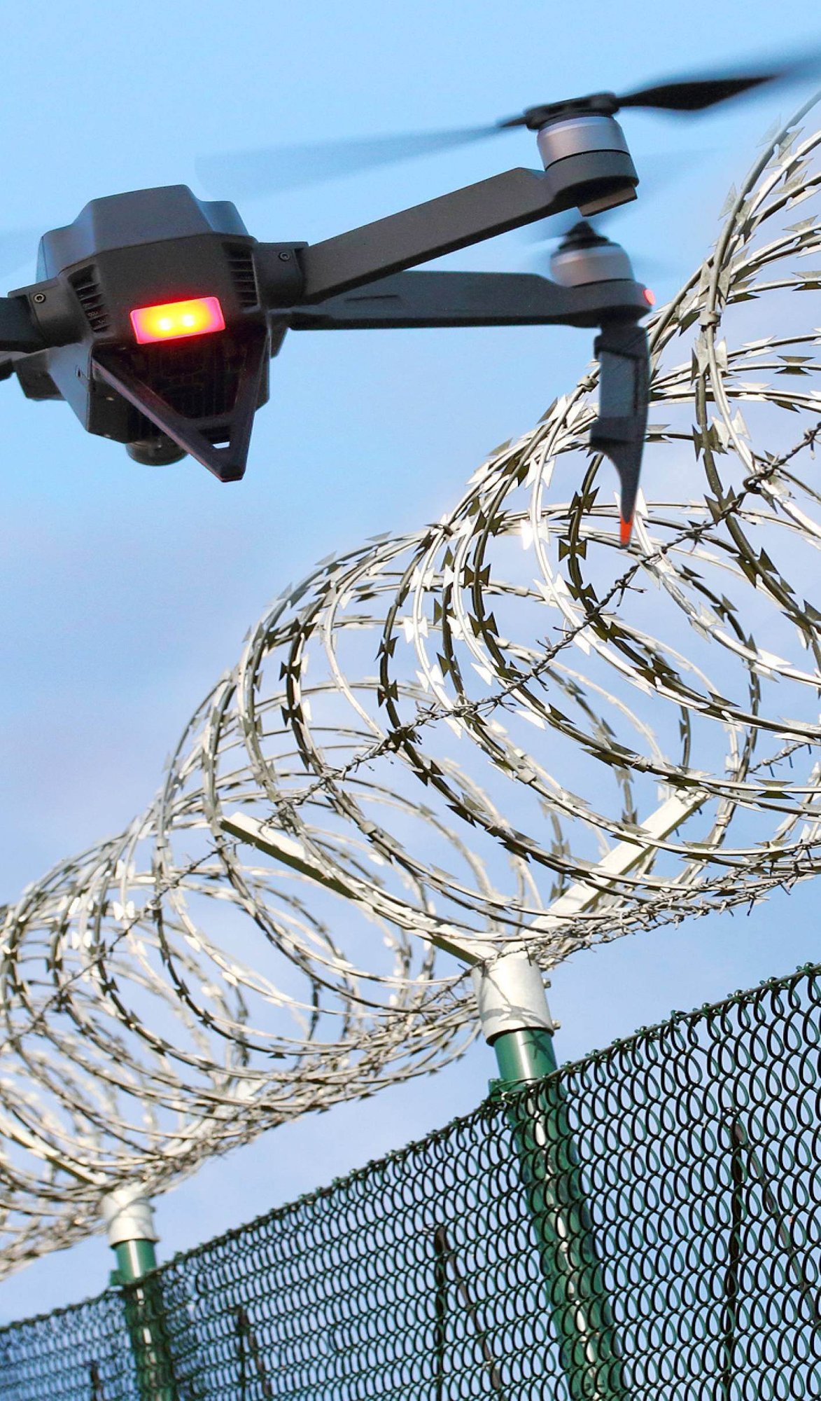 Black, quadcopter drone flying next to a razor wire fence