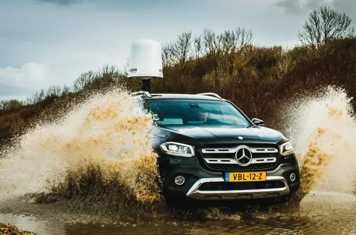 A black Mercedes 4x4 driving through a large puddle on a dirt roadwith IRIS drone detection radar mounted on the roof